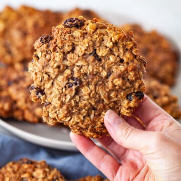 A hand holding a large healthy gluten-free oatmeal cookie.