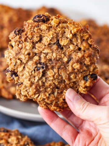 A hand holding a large healthy gluten-free oatmeal cookie.