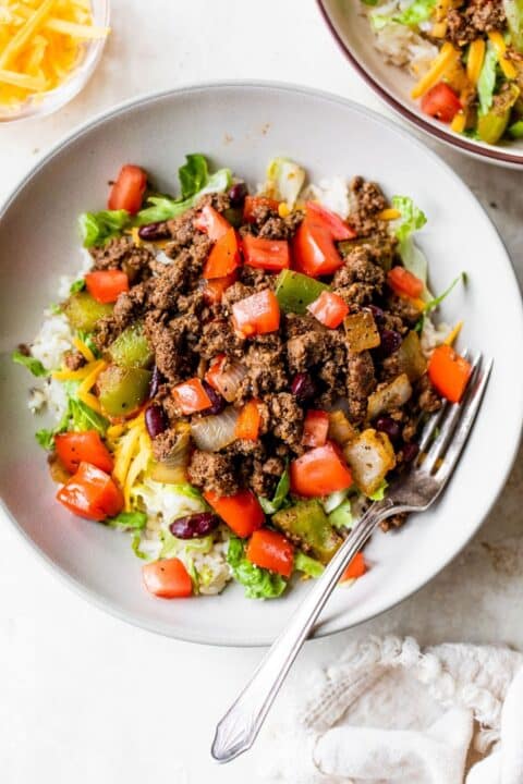 an overhead shot of bison taco bowl on a white plate with a silver fork tucked in the side.