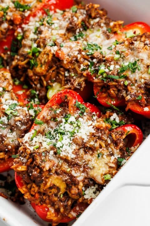 an up close shot of bison and mushroom stuffed red peppers in a white casserole dish.