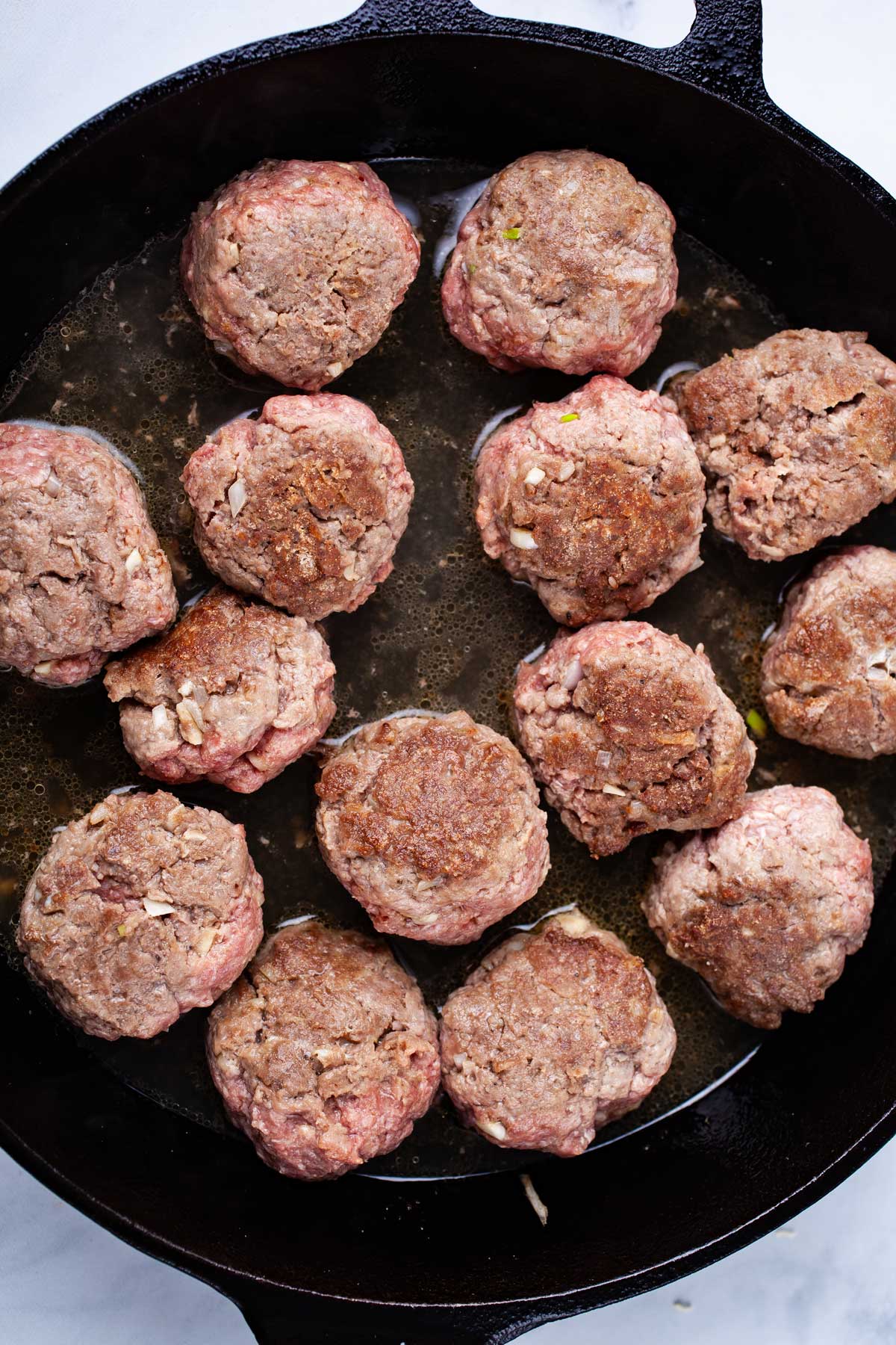 Half cooked bison meatballs in a cast iron pan.