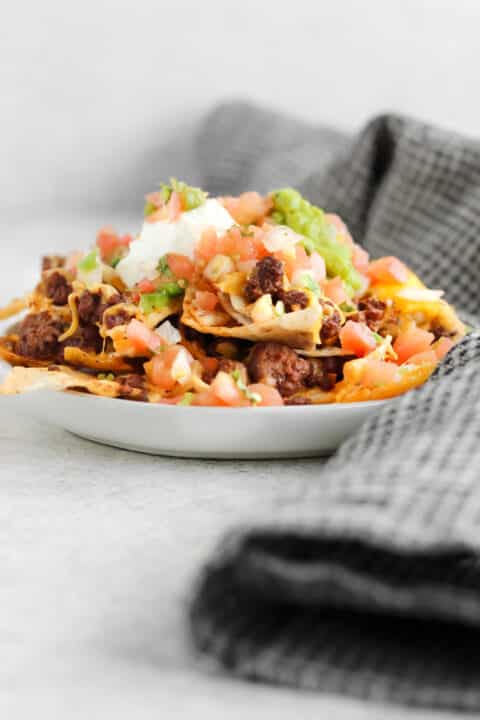a plate piled high with bison nachos topped with fresh tomatoes and cheese.