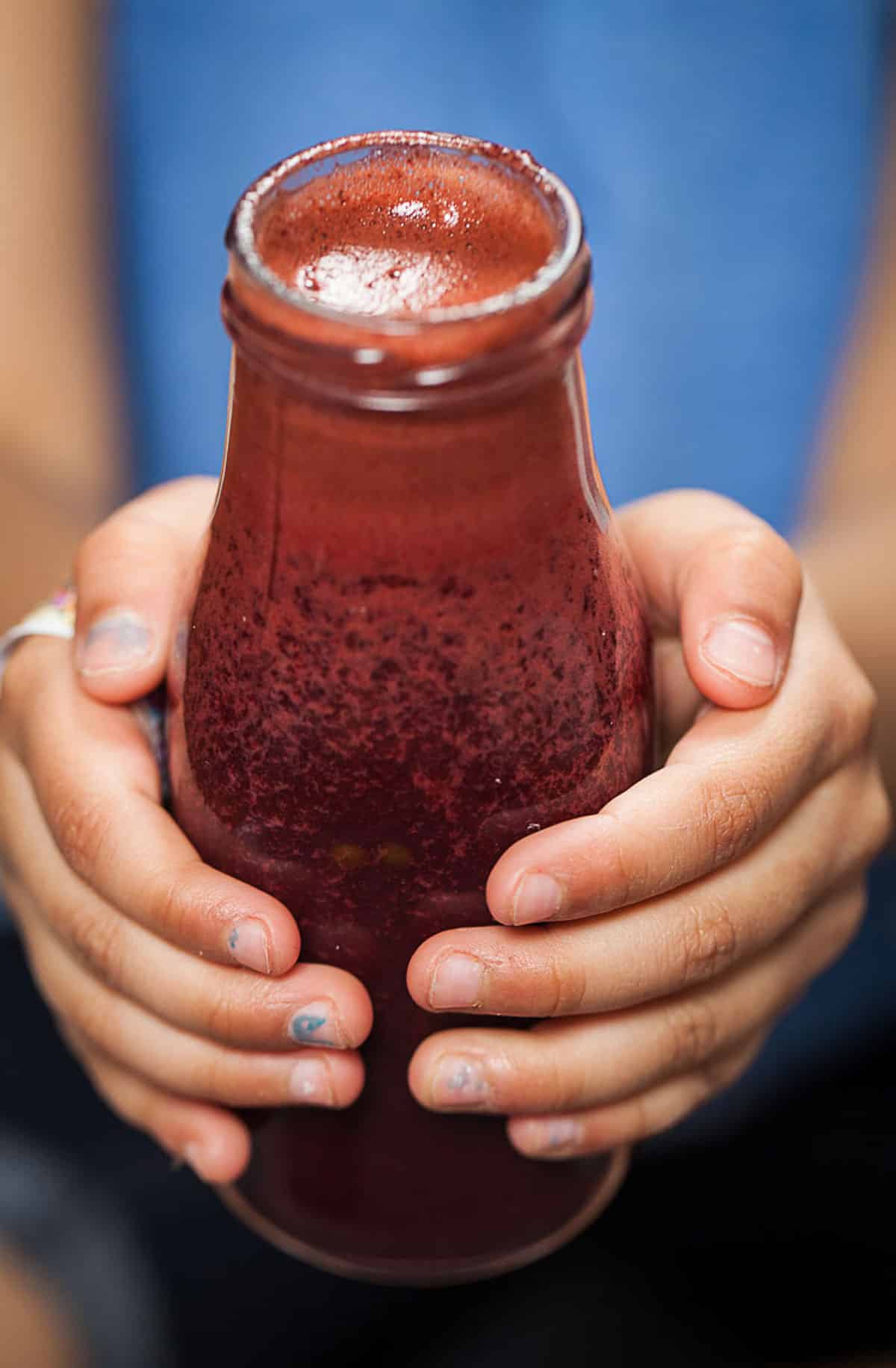 A child holding a small glass bottle with red beet juice smoothie.