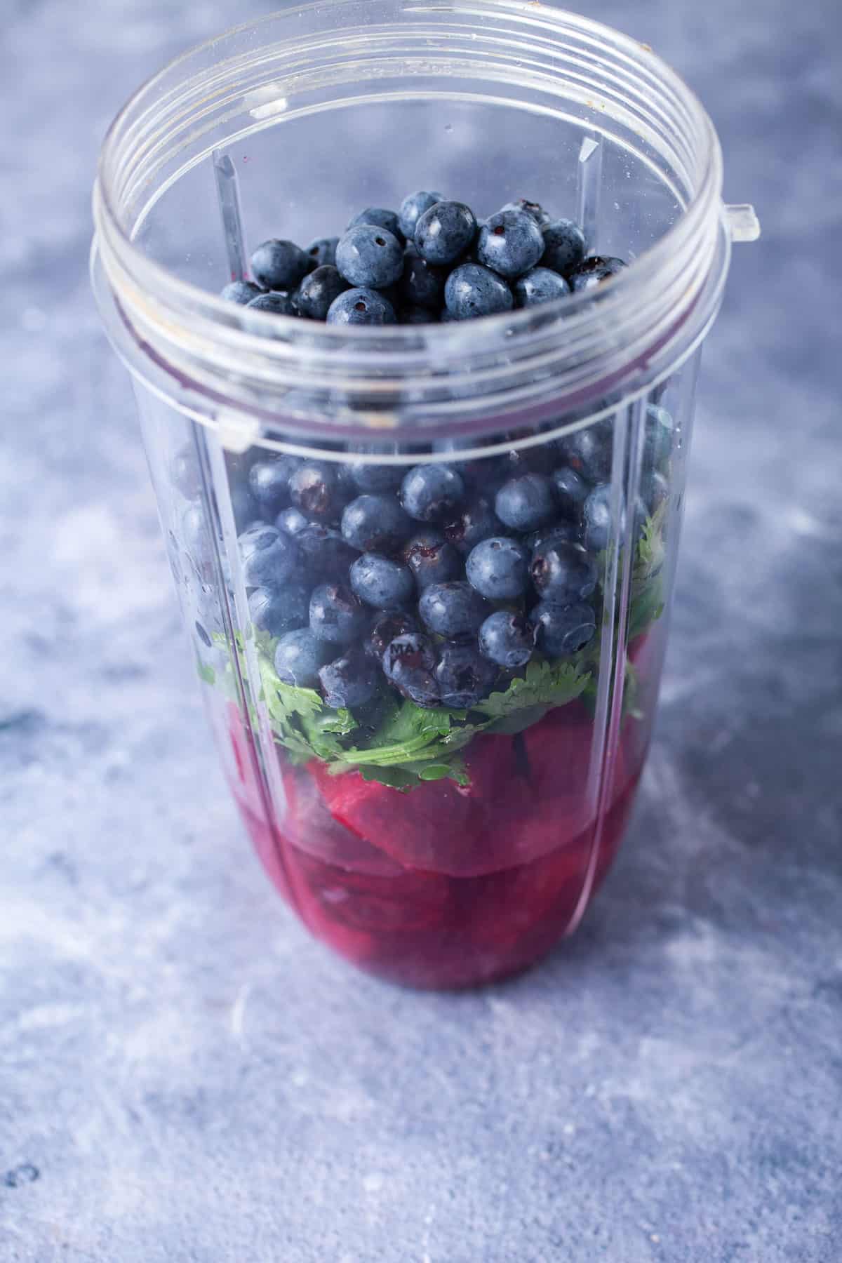 A blender filled with juice, cilantro, beets, and bleuberries.