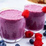 Two purple blueberry and raspberry smoothies on a table.