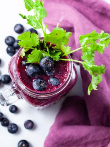 A glass of beet juice smoothie topped with blueberries and garnished with fresh cilantro leaves.