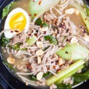 Bock choy soup with pork and noodles and garnished with chili peppers, peanuts, and hard-boiled egg.