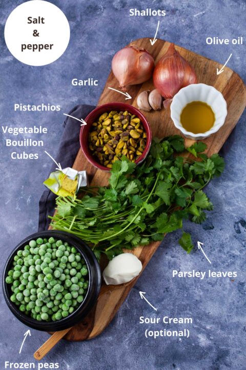 Ingredients such as salt and pepper, shallots, olive oil, garlic, pistachios, vegetable bouillon cubes, fresh parsley leaves, sour cream, and frozen peas to make soup.