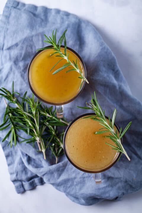 Two cups of bone broth drinks garnished with fresh Rosemary sprigs.