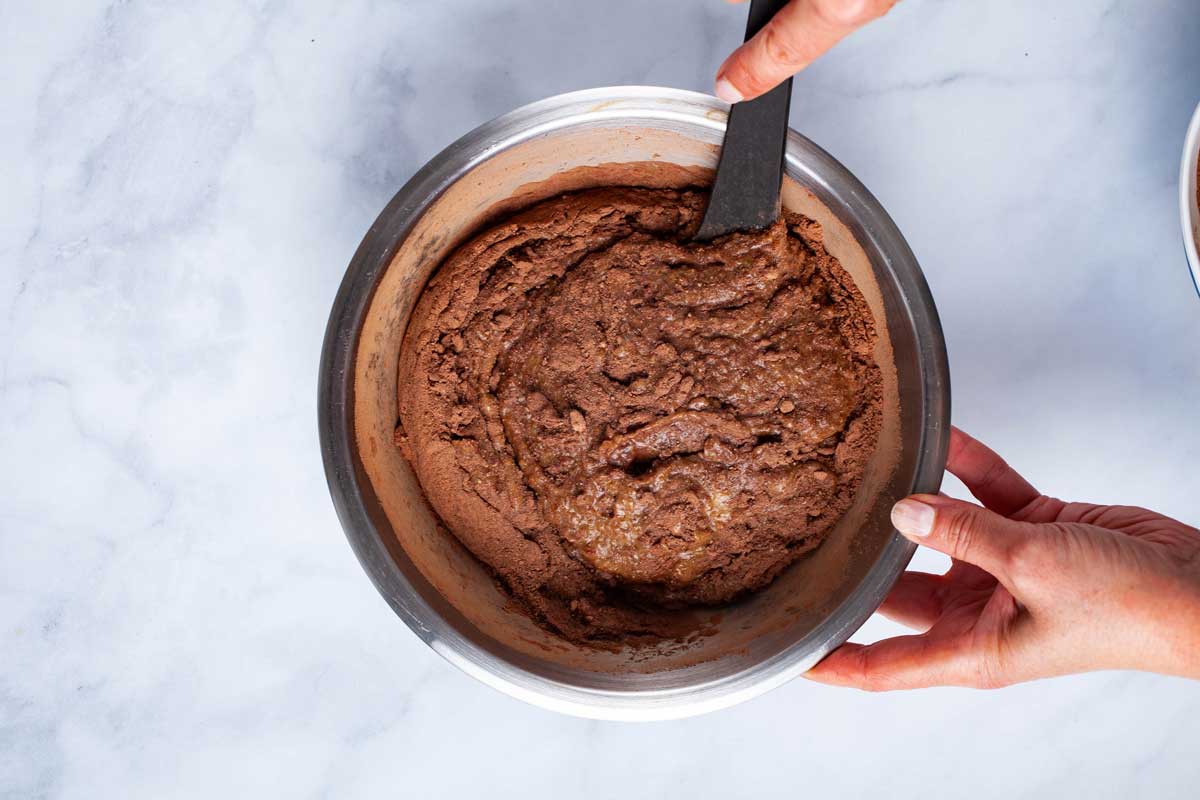 A hand stirring in a bowl with chocolate brownie batter.
