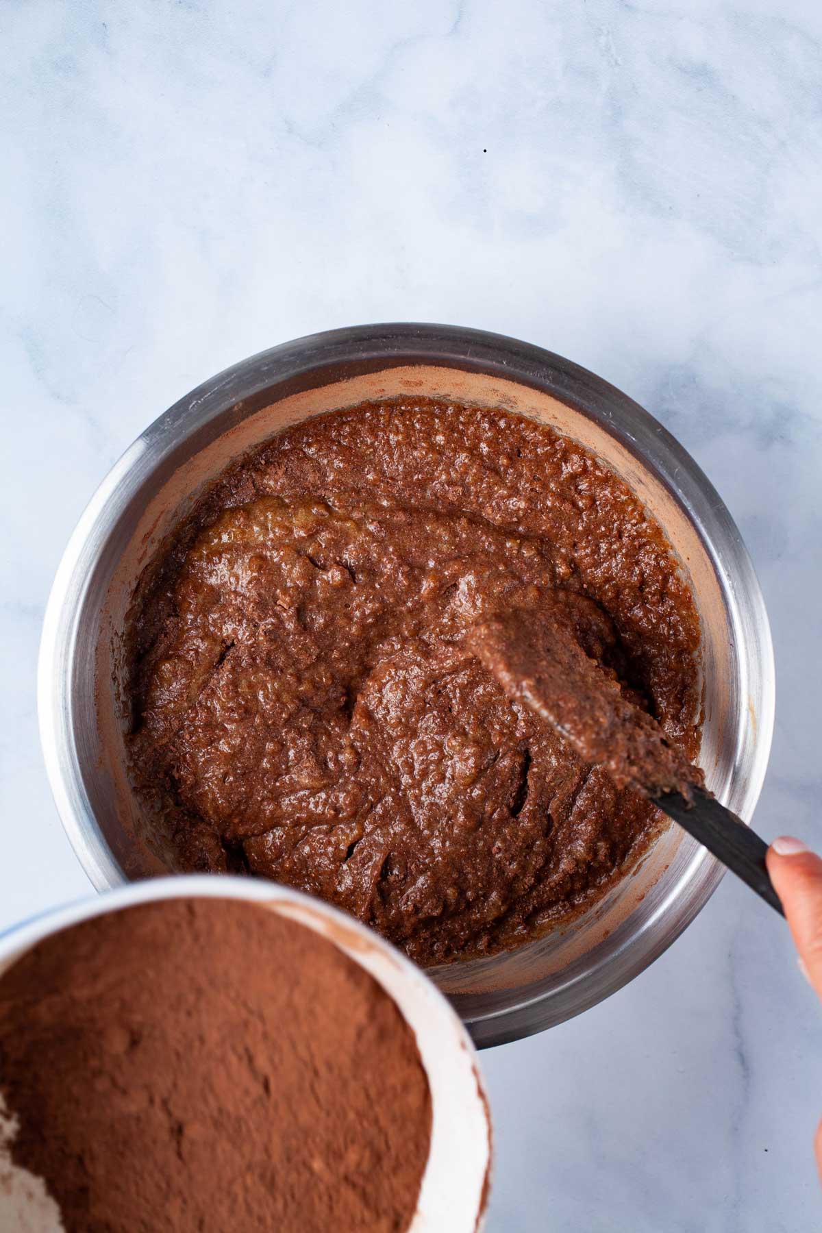 A hand folding in cocoa powder into a date paste.