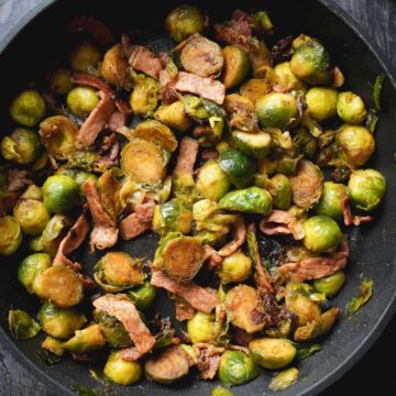 Caramelized Brussels Sprouts with bits of bacon in a large pan.