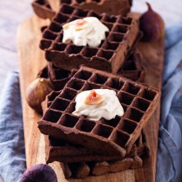 Buckwheat waffles topped with a dollop of yogurt and fresh figs served on a wooden board.