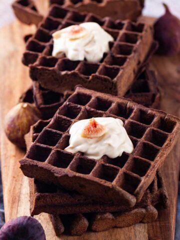 Buckwheat waffles topped with a dollop of yogurt and fresh figs served on a wooden board.