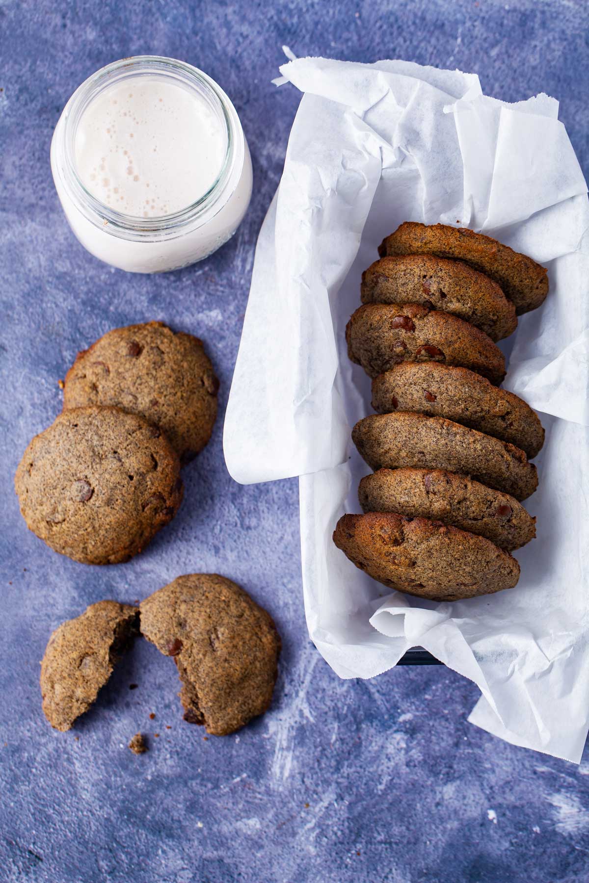 A basket filled with buttery buckwheat cookies, next to a cup of milk and some cookies spread out on the table.