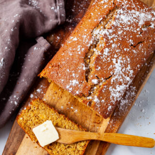 A sliced quick bread on a wooden board with butter on knife.