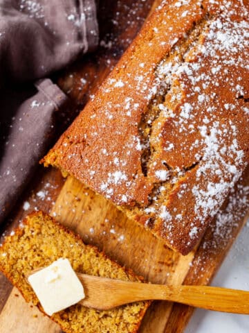 A sliced quick bread on a wooden board with butter on knife.