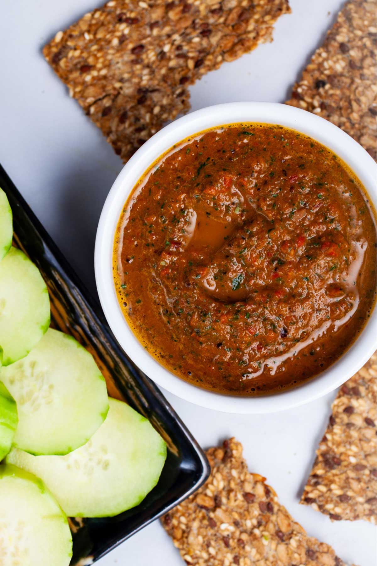 An Italian red pepper spread in a ramekin next to cucumber slices and toast.