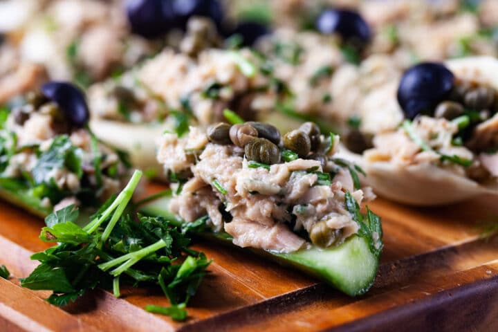 A close up of a thick fresh cucumber slice topped with creamy tuna salad and garnished with fresh parsley and green capers.