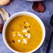 Orange soup in a white bowl topped with shaved almonds and chili flakes.