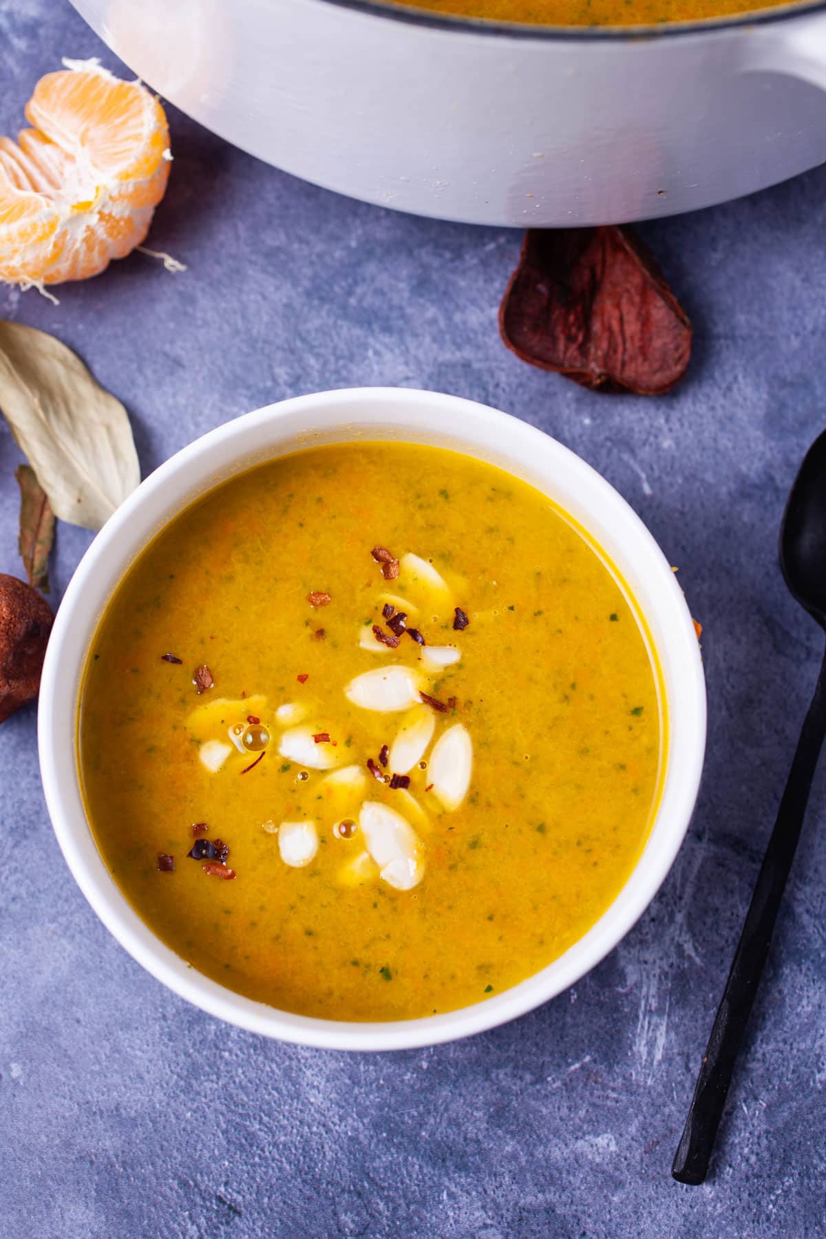 Orange soup in a white bowl topped with shaved almonds and chili flakes.