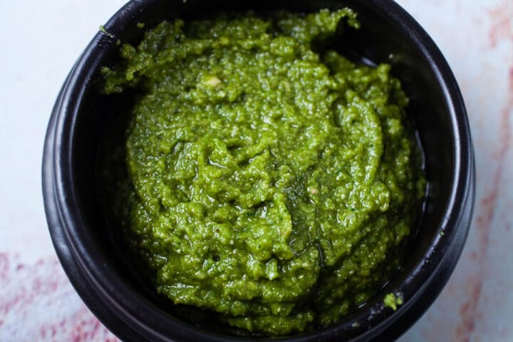 A beautiful green pesto sauce presented in a black bowl.