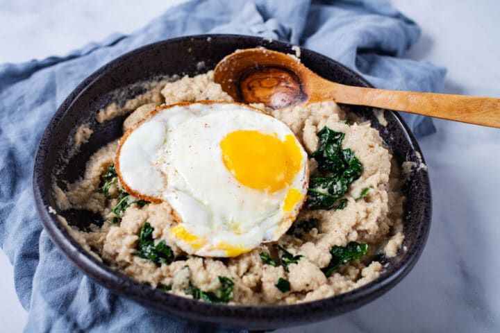 A bowl filled with a kale and cauliflower mash, topped with an egg sunny side up.