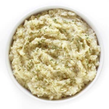 Mashed celery root in a serving bowl and topped with herbs.