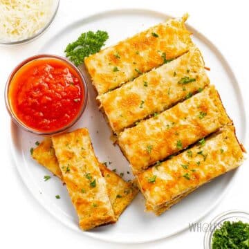 Cauliflower breadsticks on a plate next to a tomato-based sauce.