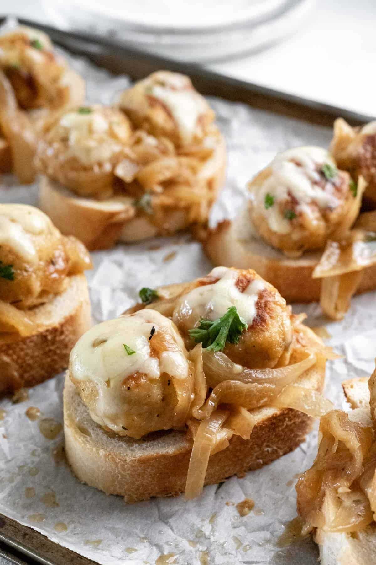 Meatballs topped with caramelized onions and served on sliced baguette as an appetizer.