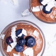 Two mini cups with blended chocolate chia mousse and topped with blackberries and coconut shreds.