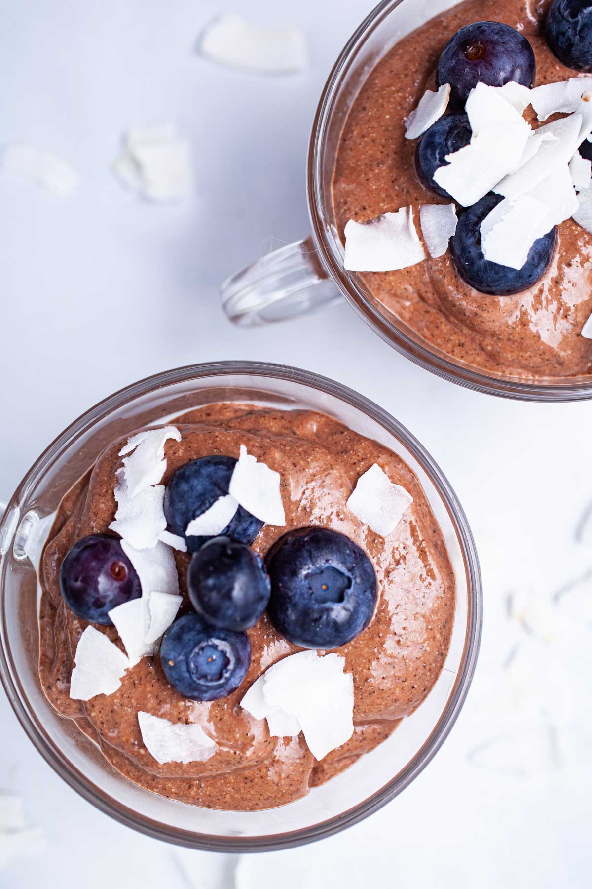 Two mini cups with blended chocolate chia mousse and topped with blackberries and coconut shreds.