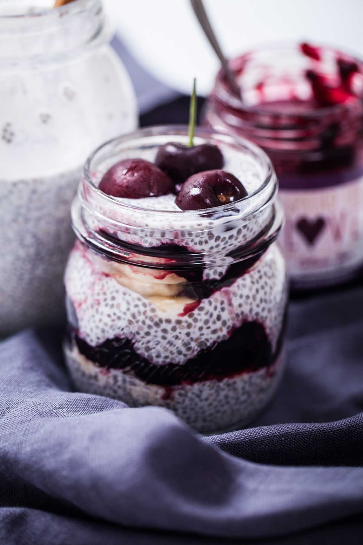 A cherry, banana, and jam layered chia seed pudding in a jar.