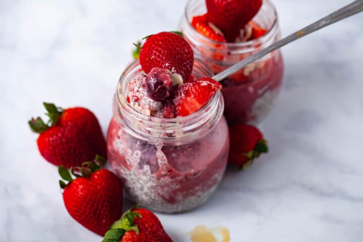 Two small jars filled with chia pudding, infused with a berry sauce, and topped with fresh strawberries.