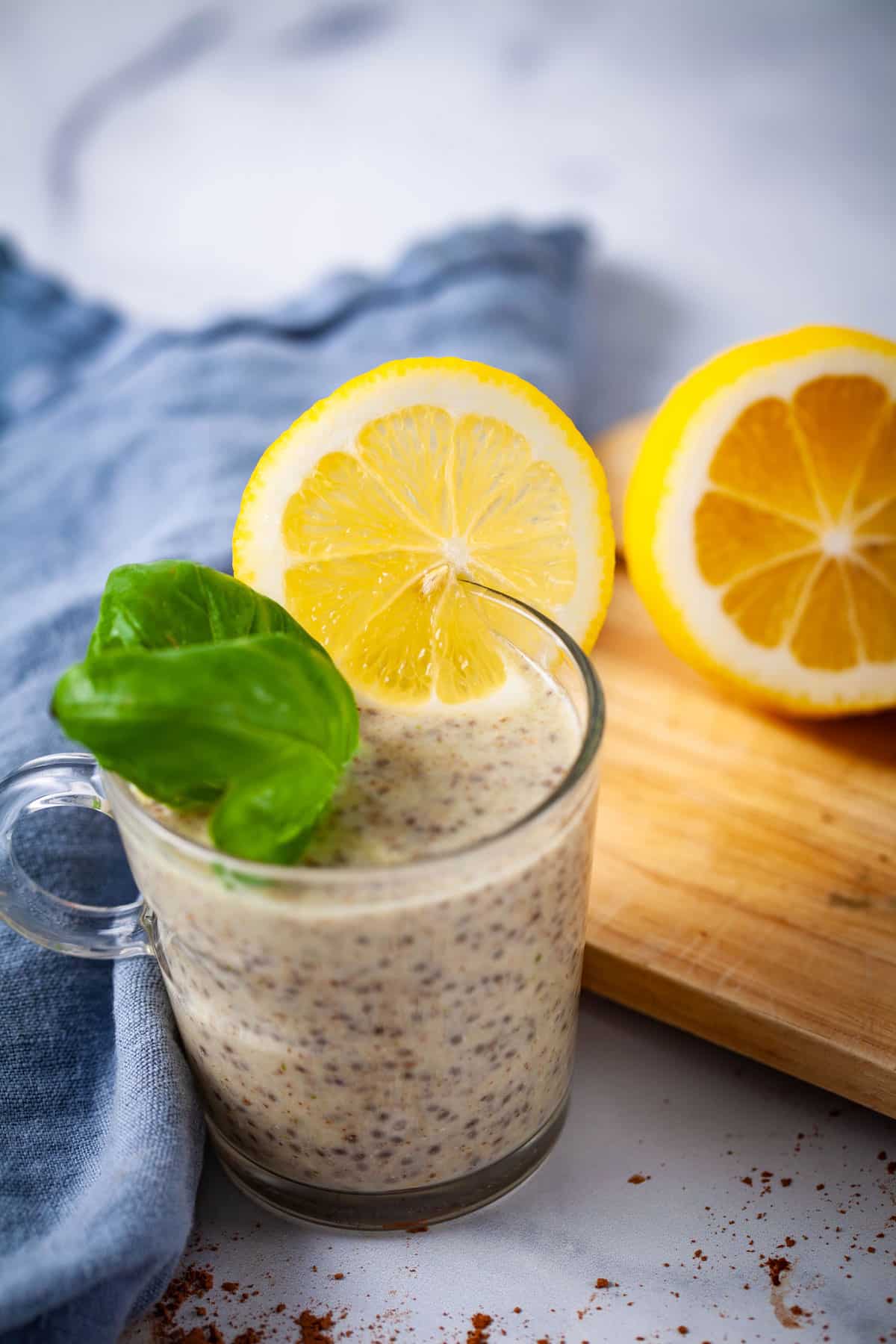 A small glass cup filled with chia pudding and topped with fresh Basil leaves and a slice of lemon.