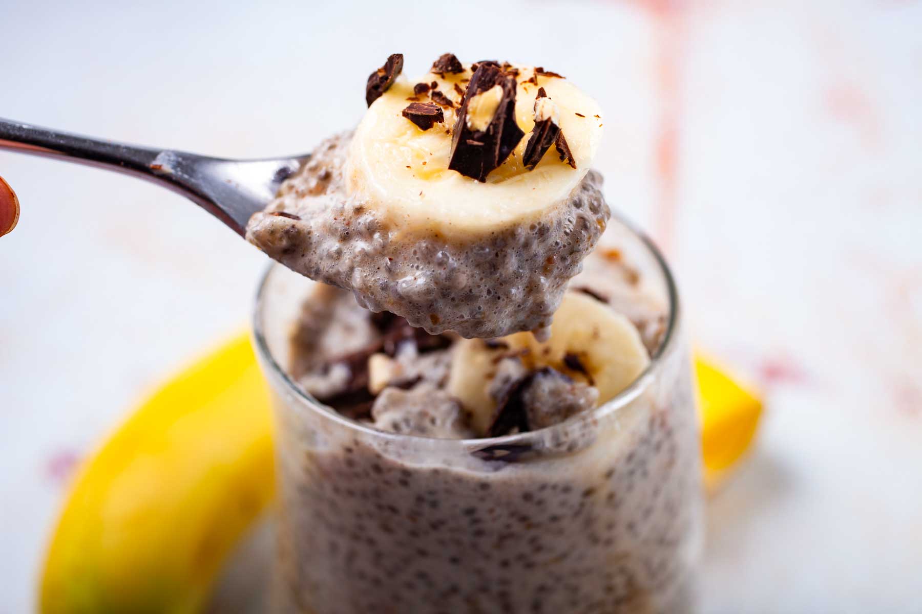 A hand holding a fill spoon of banana chia pudding over a cup.