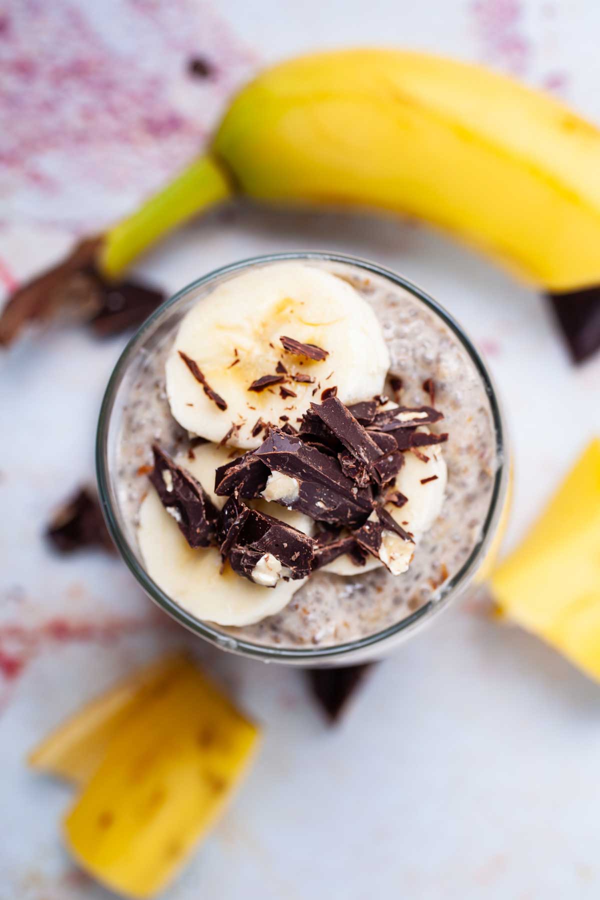 A cup full of banana chia pudding topped with fresh banana slices and shaved chocolate.