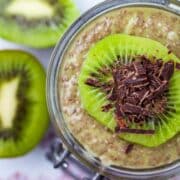 A cup filled with kiwi chia pudding topped with a slice of fresh kiwi fruit and shaved chocolate.