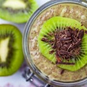 A cup filled with kiwi chia pudding topped with a slice of fresh kiwi fruit and shaved chocolate.