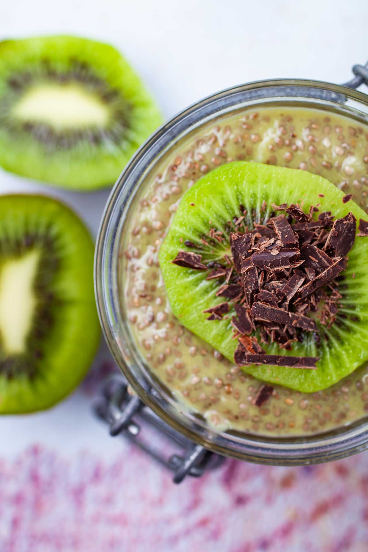 A cup filled with kiwi chia pudding topped with a slice of fresh kiwi fruit and shaved chocolate.