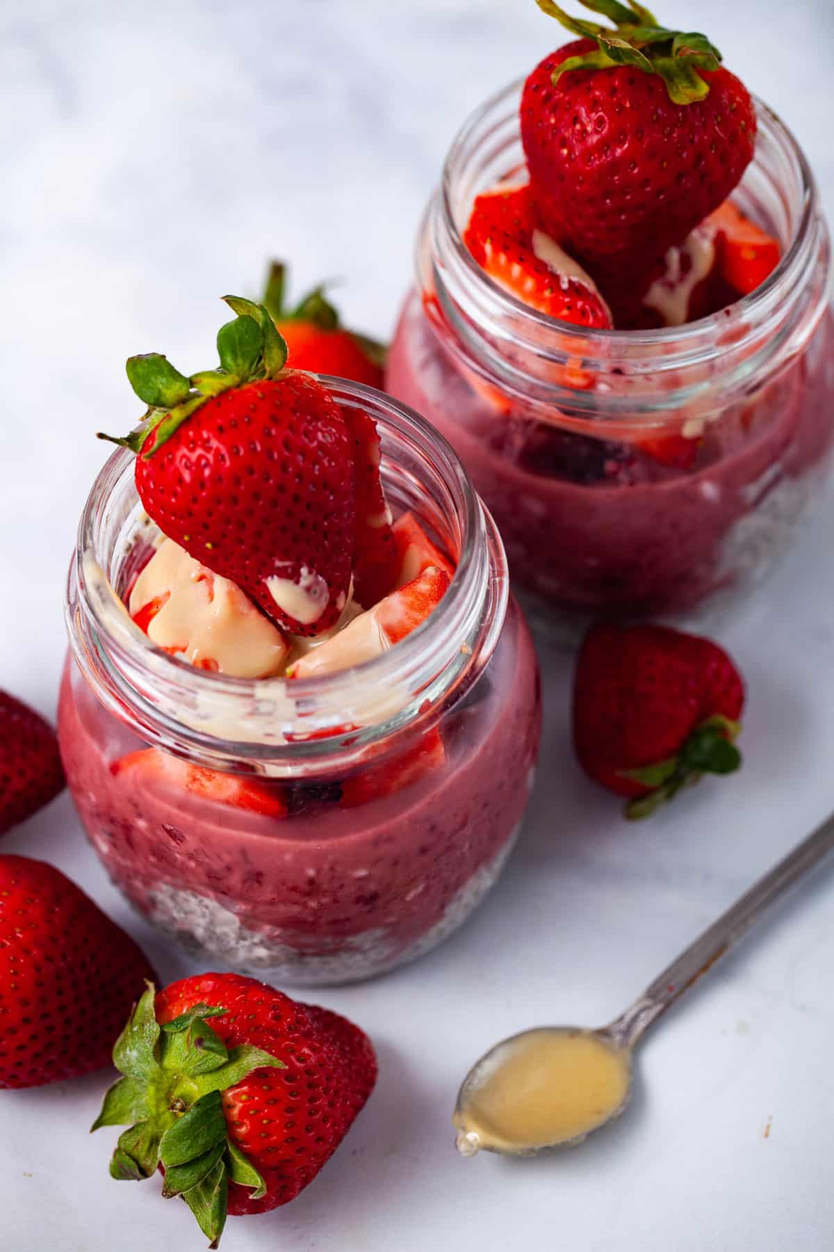Two small jars filled with chia pudding, infused with a berry sauce, and topped with fresh strawberries and a drizzle of Tahini butter.