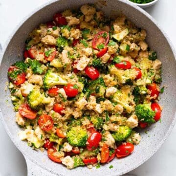 Quinoa and chicken coated with broccoli, tomatoes and herbs, served in a bowl.