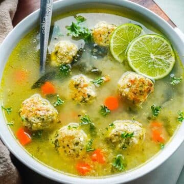 Quinoa meatballs dunked in a chicken broth soup and served with slices of lime.