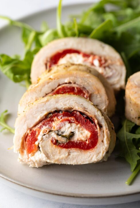 an up close shot of slice of a stuffed chicken roulade on a white plate with a bed of arugula underneath.