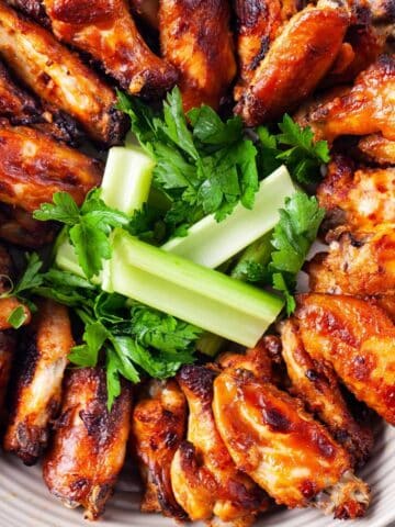 A plate neatly filled with baked chicken wings and garnished with celery and parsley.