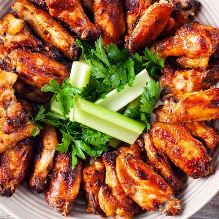 A plate neatly filled with baked chicken wings and garnished with celery and parsley.