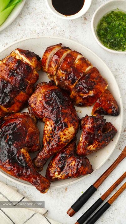 an overhead shot of pieces of chinese five spice chicken beautifully browned on a white plate with a bowl of green herb sauce on the side.