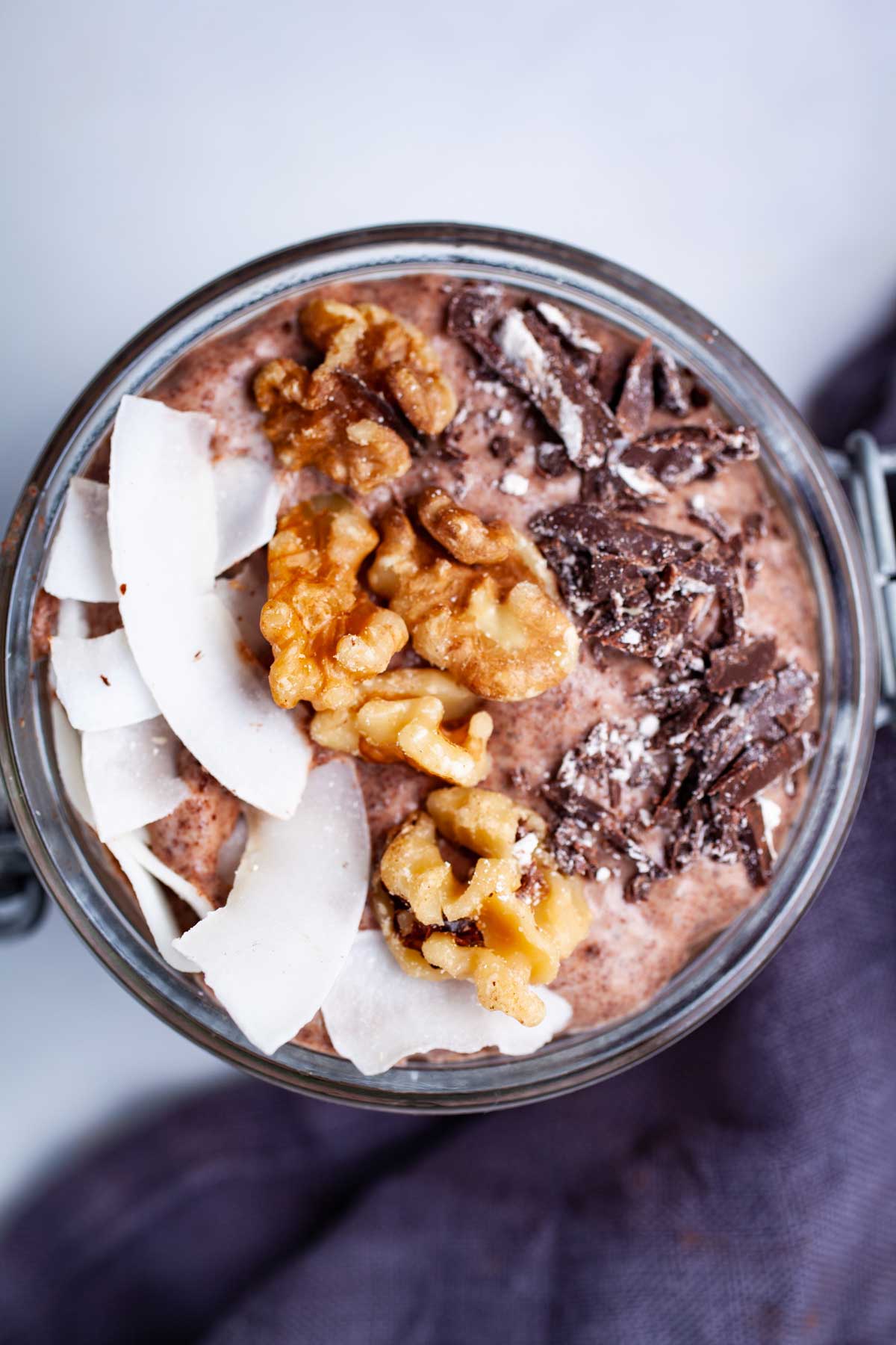 A chocolate chia pudding in a mason jar topped with coconut flakes, walnuts, and dark chocolate bits.