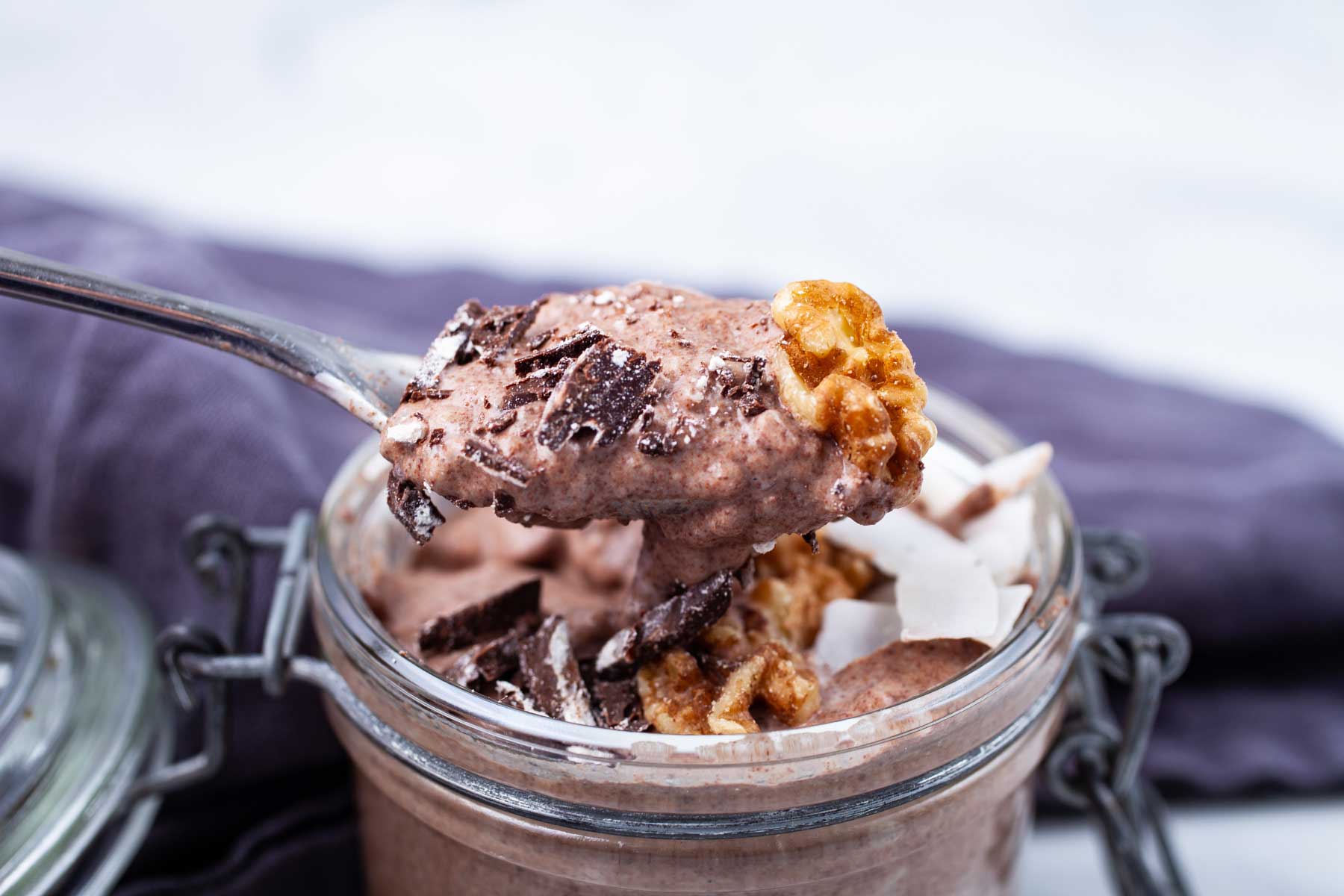 A spoon taking a bite out of a Keto chocolate chia pudding topped with walnuts and bits of dark chocolate.