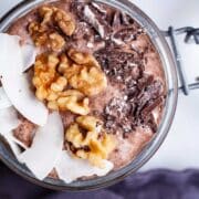 A chocolate chia pudding in a mason jar topped with coconut flakes, walnuts, and dark chocolate bits.
